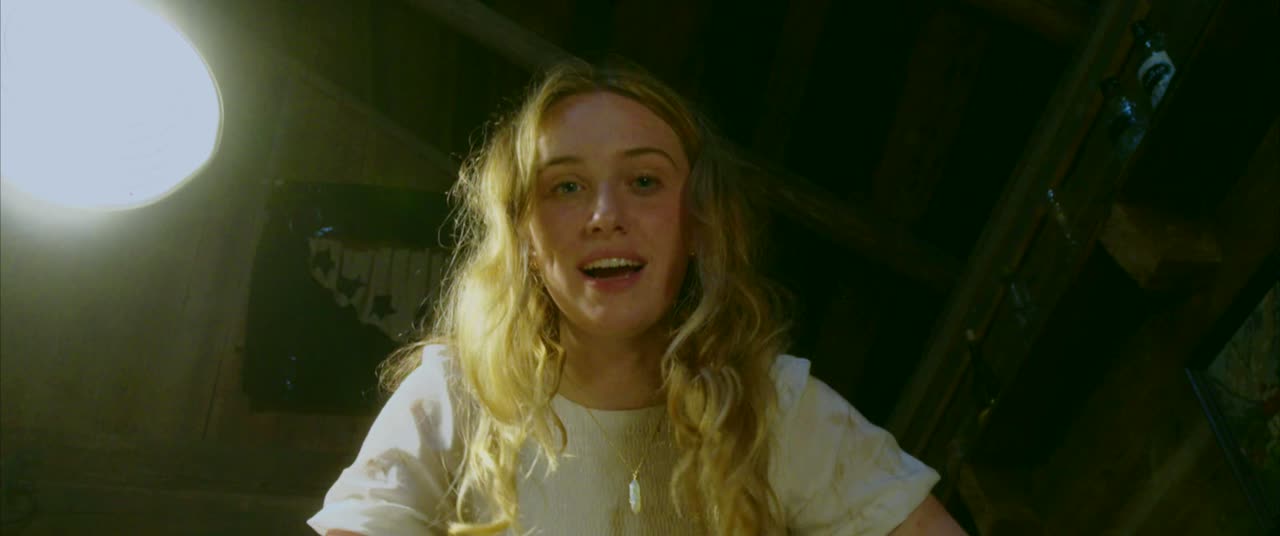 A girl in a white shirt looks down at the camera under a bare light