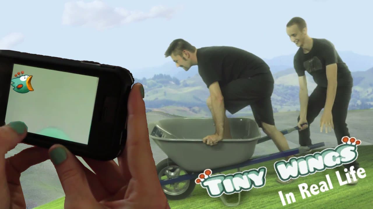 Two men pushing a wheelbarrow beside a phone playing Tiny Wings